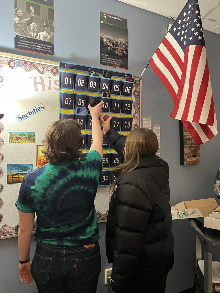 Brighton High School students Delaney Mullally (left) and Lily Storey (right) collect their cell phones from a cell phone pocket after class.