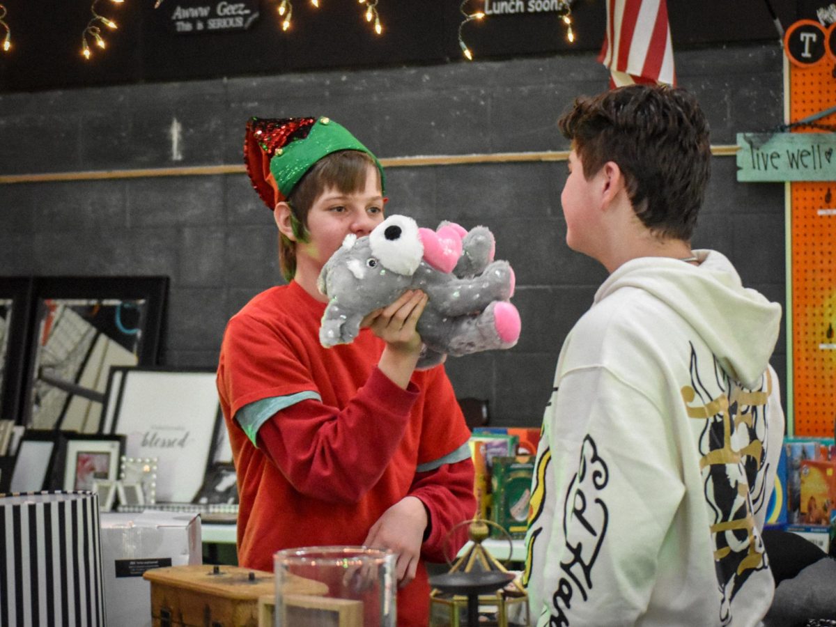 Sophomore Cully Johnson holds up a product to a customer at a holiday-themed garage sale hosted by Brighton High School's Transition Into Post-Secondary program.